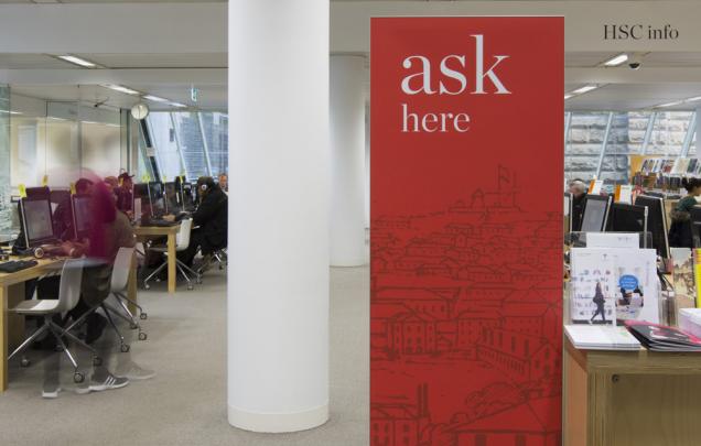 Large ASK sign in front of people on computers and at tables
