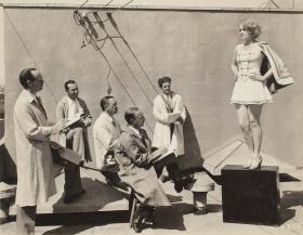 Several men in white coats sketching a young woman modelling