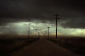 A photograph looking down a road lined with electricity poles - the air is coloured grey and yellow by particles in the air.