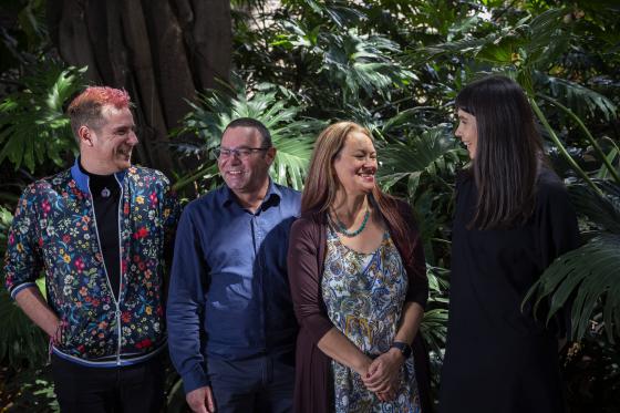 Two men and two women representing the Indigenous Engagement Branch smiling and standing in front of green plants.