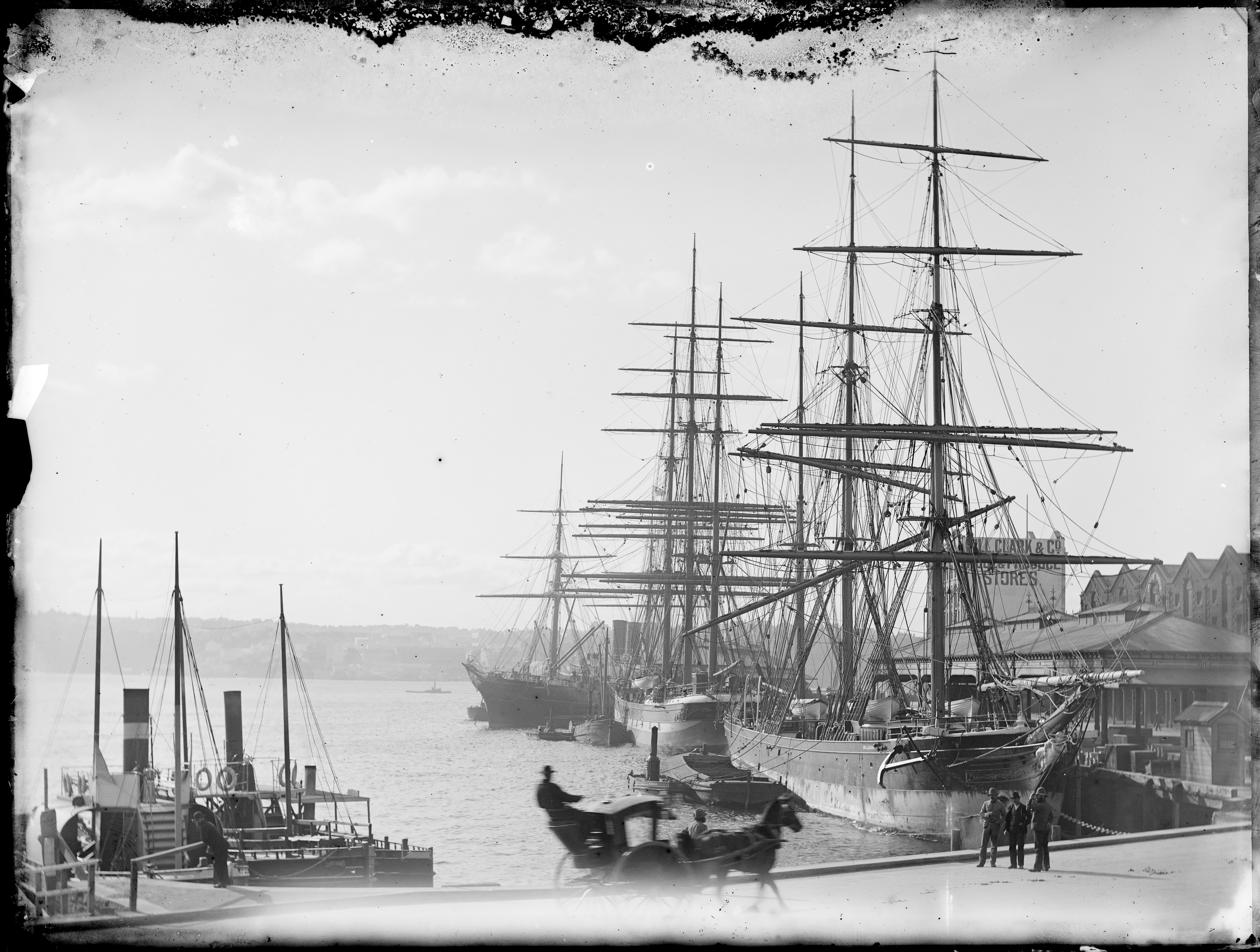 Black and white photograph of tall ships moored in a harbour. 