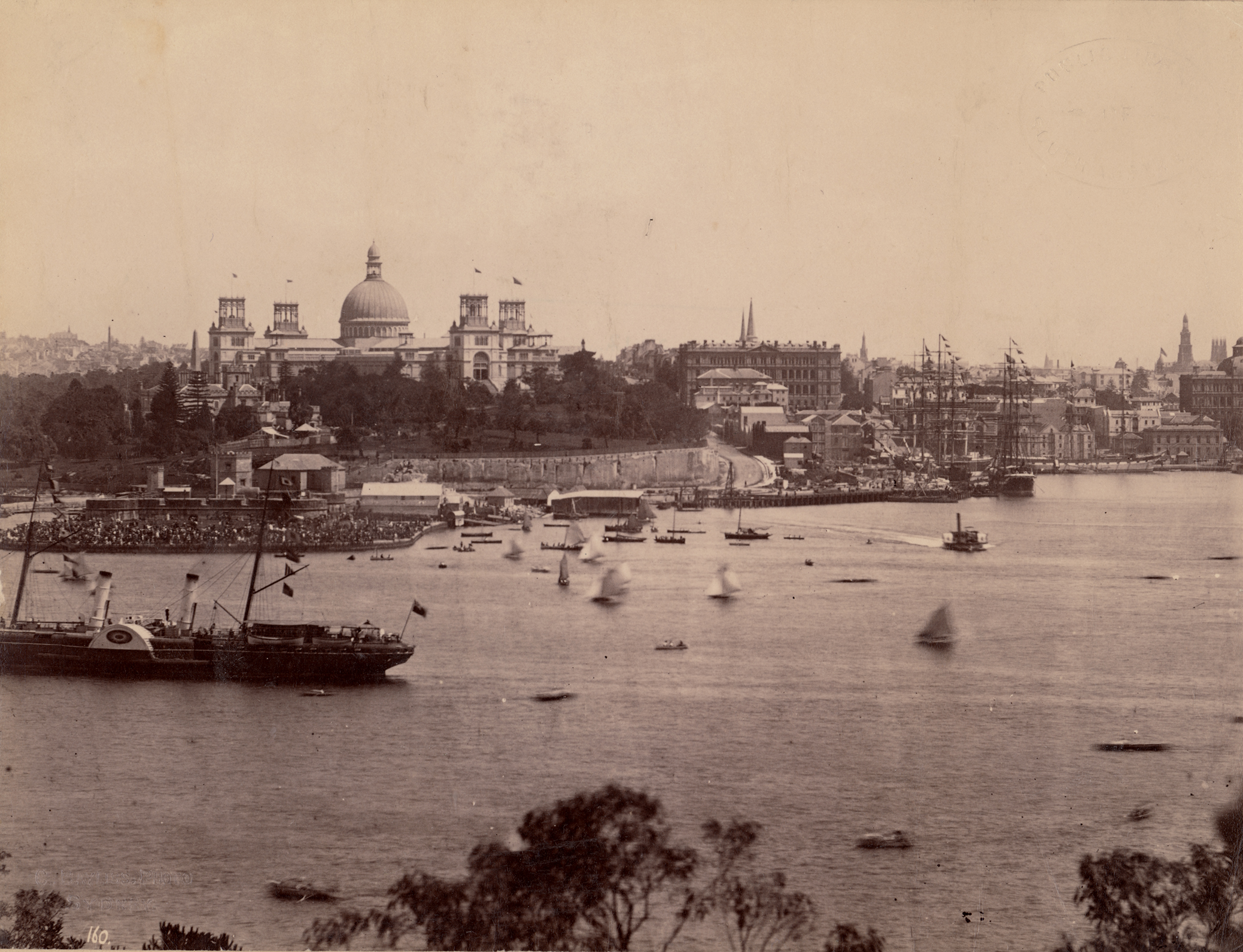A sepia photograph of the Garden Palace taken from the north side of Sydney Harbour looking back across the harbour with tall ships in Circular Quay