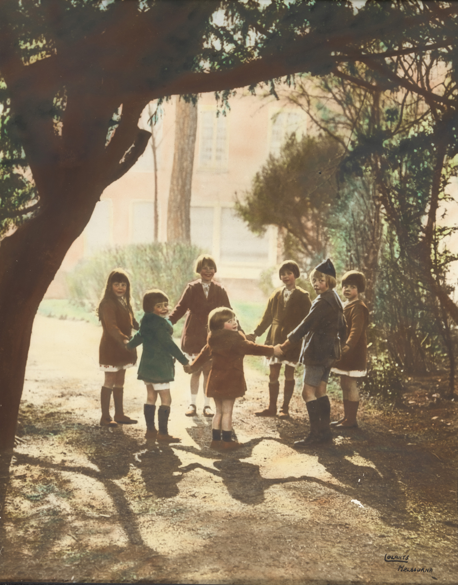 A hand coloured photograph of children holding hands in a circle. 