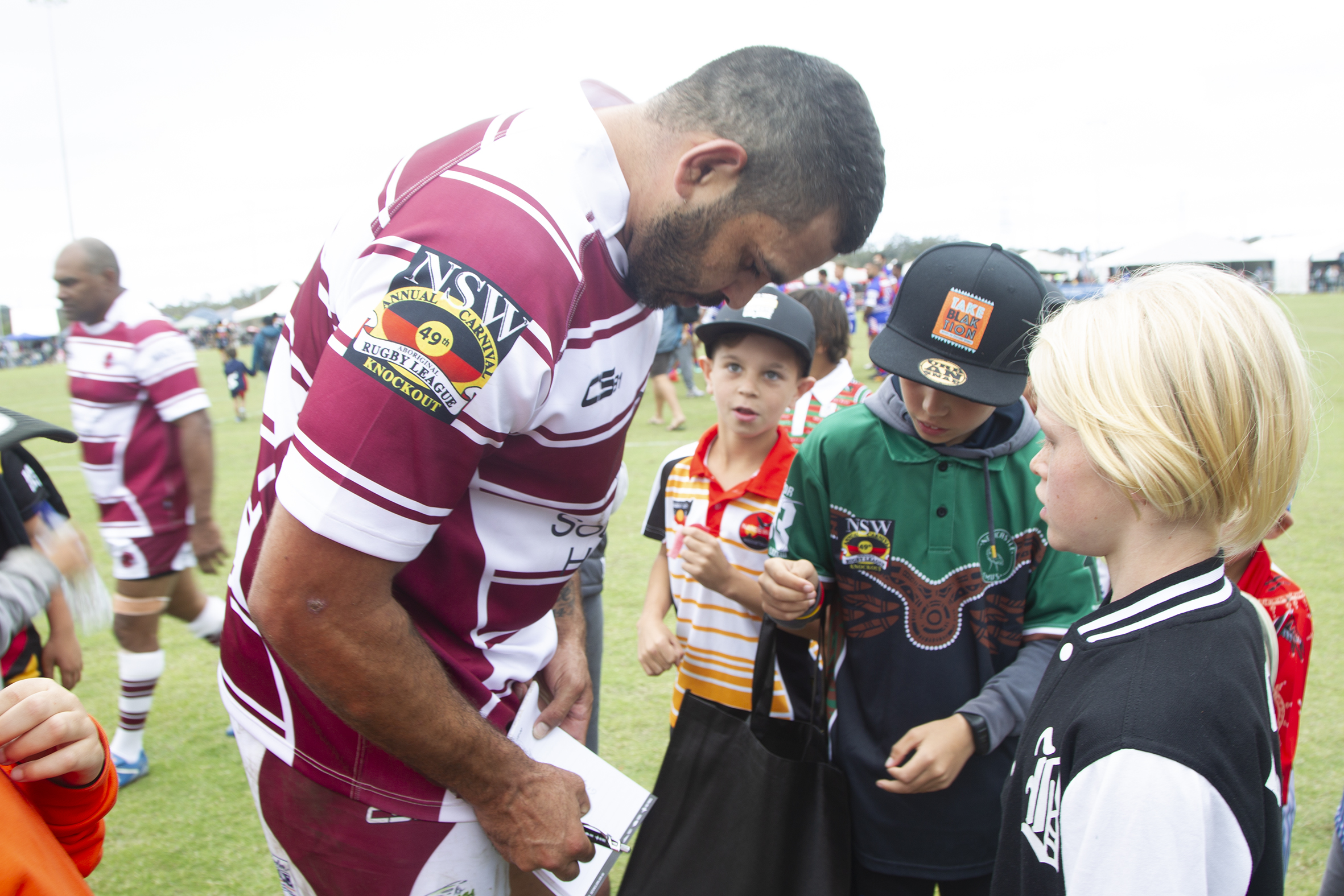 Player Greg Inglis signs autographs for fans on sports field at Tuggerah