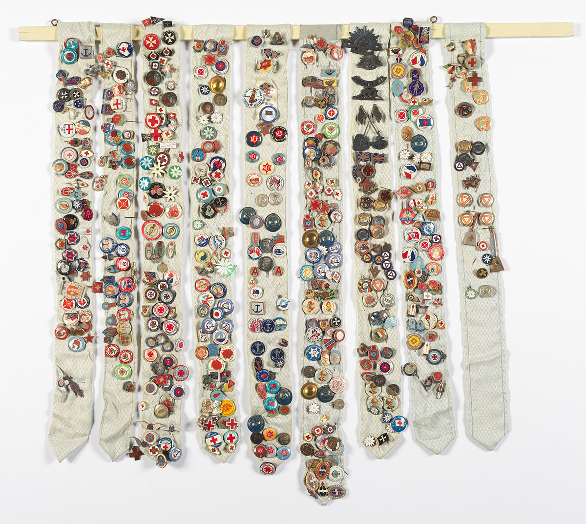 Photograph of 9 long strips of fabric holding hundreds of colourful badges. 
