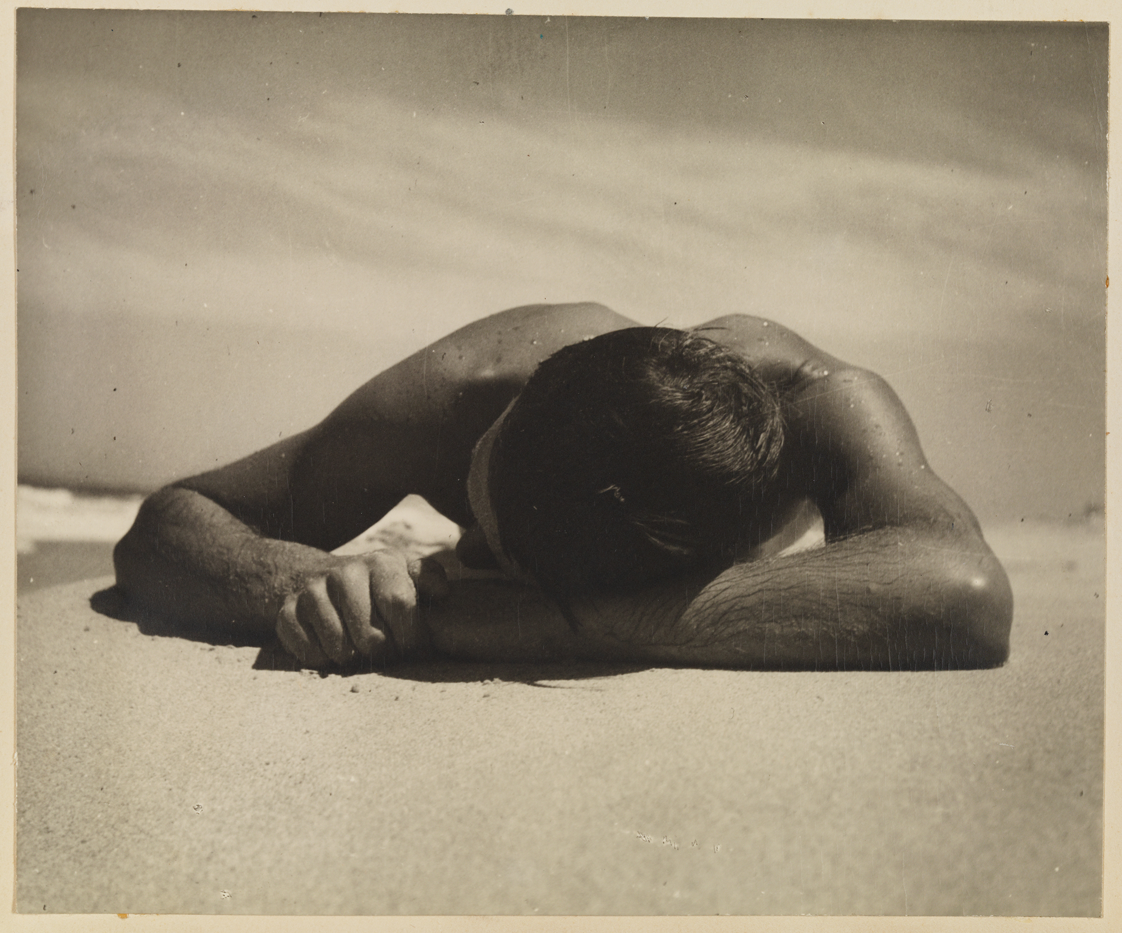 A sepia photograph of a man lying on a beach, covered in droplets of water