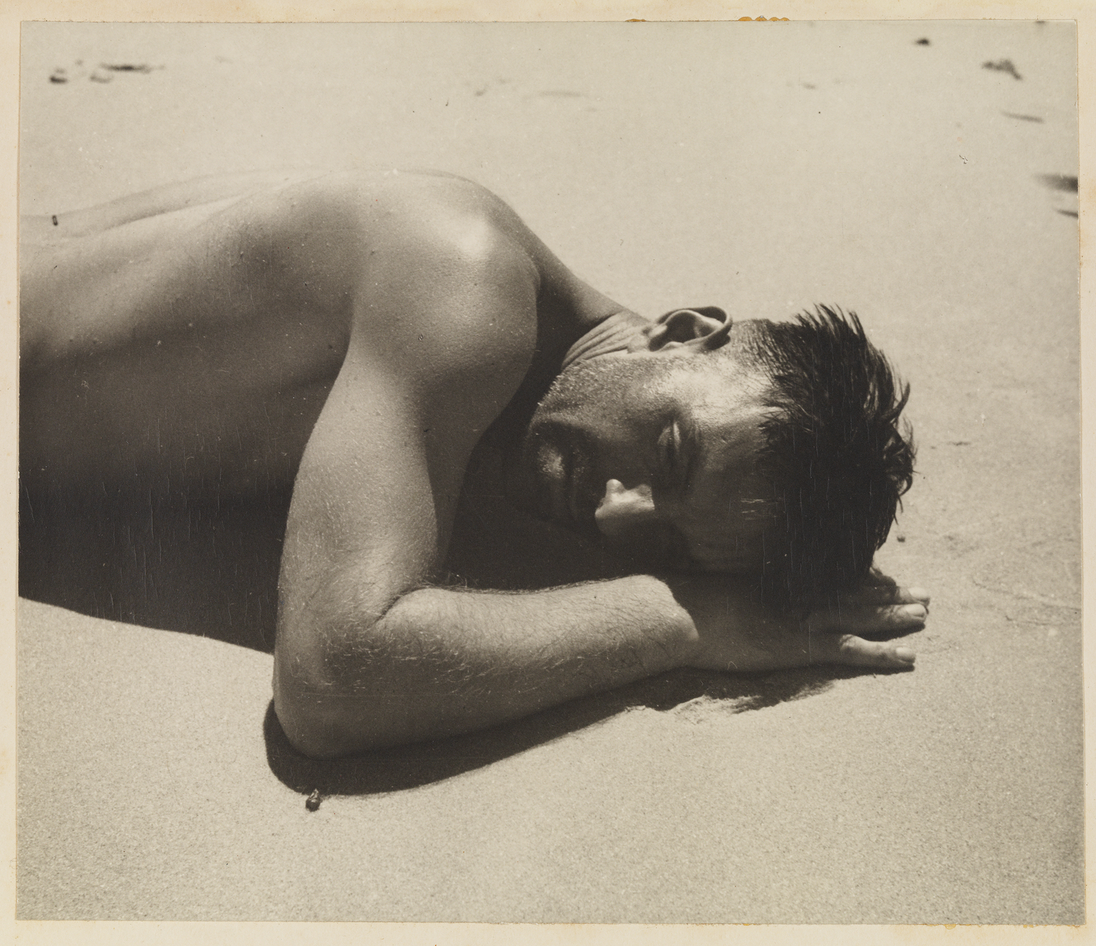 A sepia photograph of a man lying on a beach, covered in droplets of water