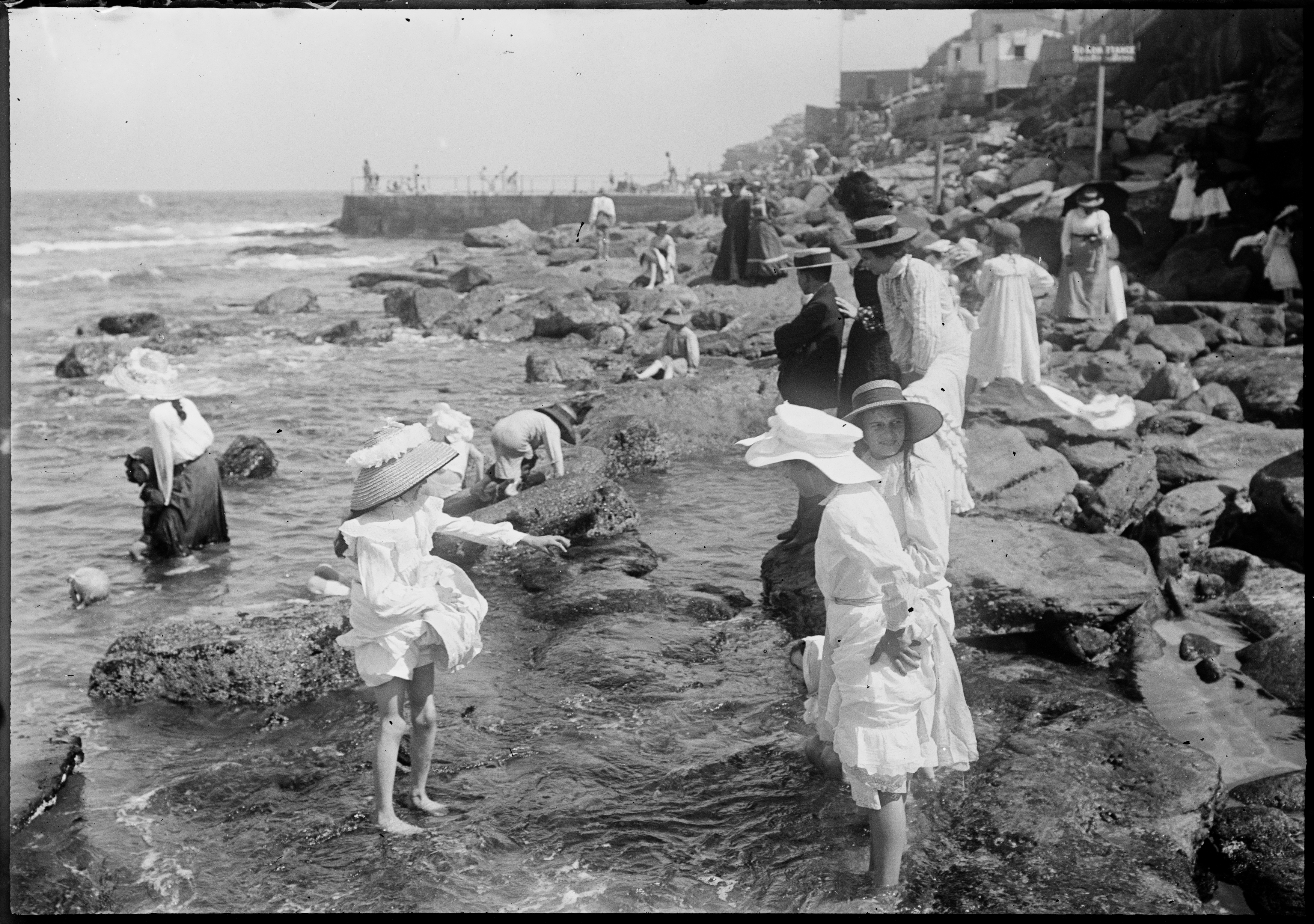 Children paddling in rock pools with swimming baths behind, South Bondi
