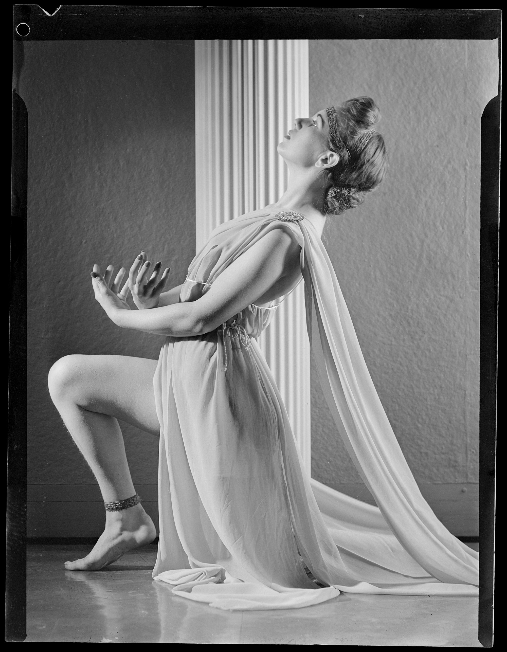 Black and white photo of Charmian Clift in a Grecian dress posing 