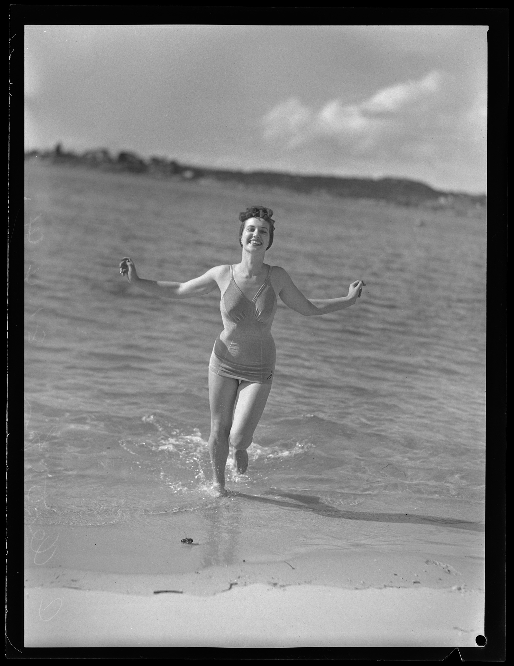 Black and white photograph of Charmian Clift running up the beach.