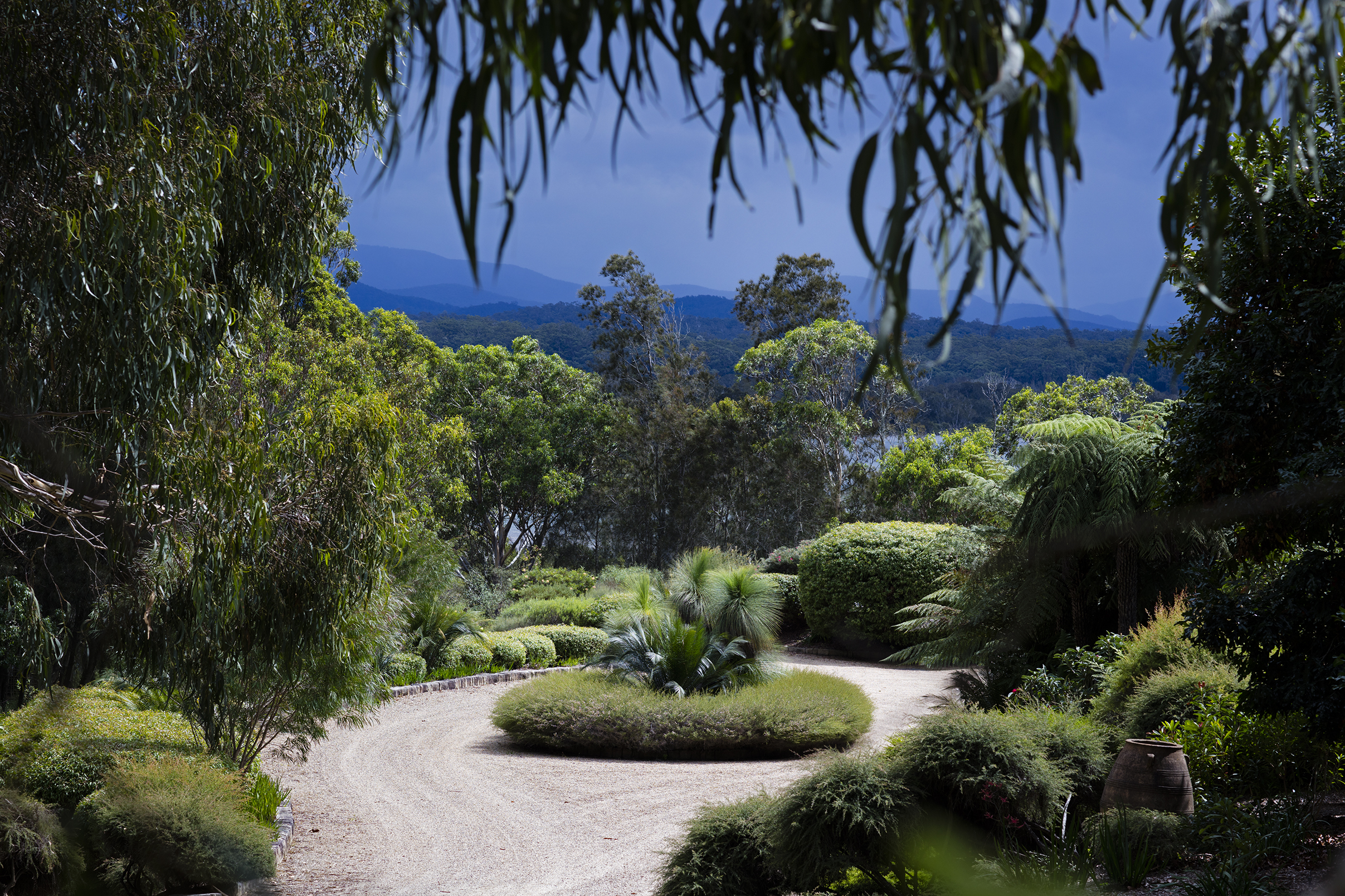 A circular driveway framed by foliage with a view in the distance of a river and mountain range. 