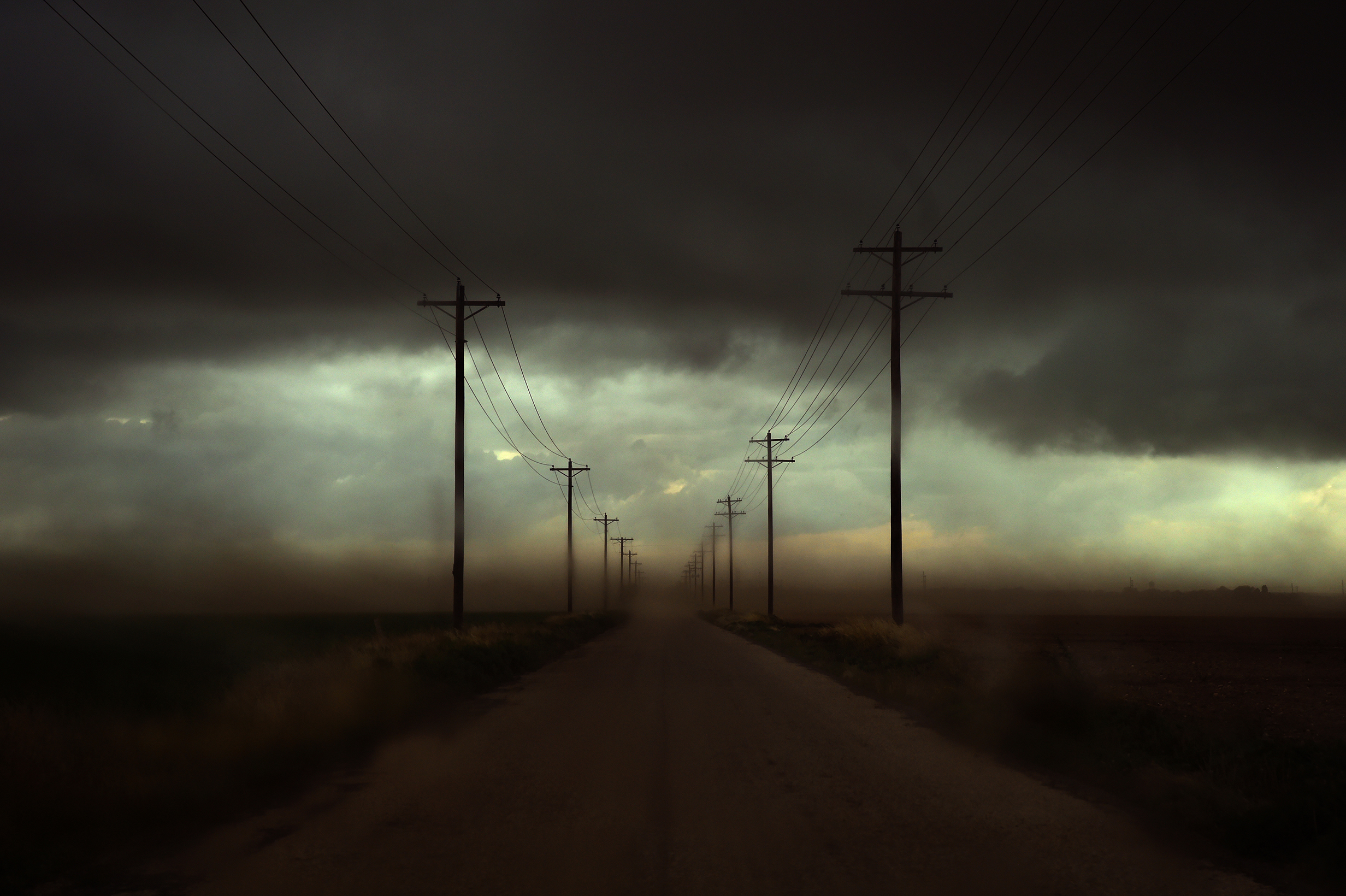 A photograph looking down a road lined with electricity poles - the air is coloured grey and yellow by particles in the air.