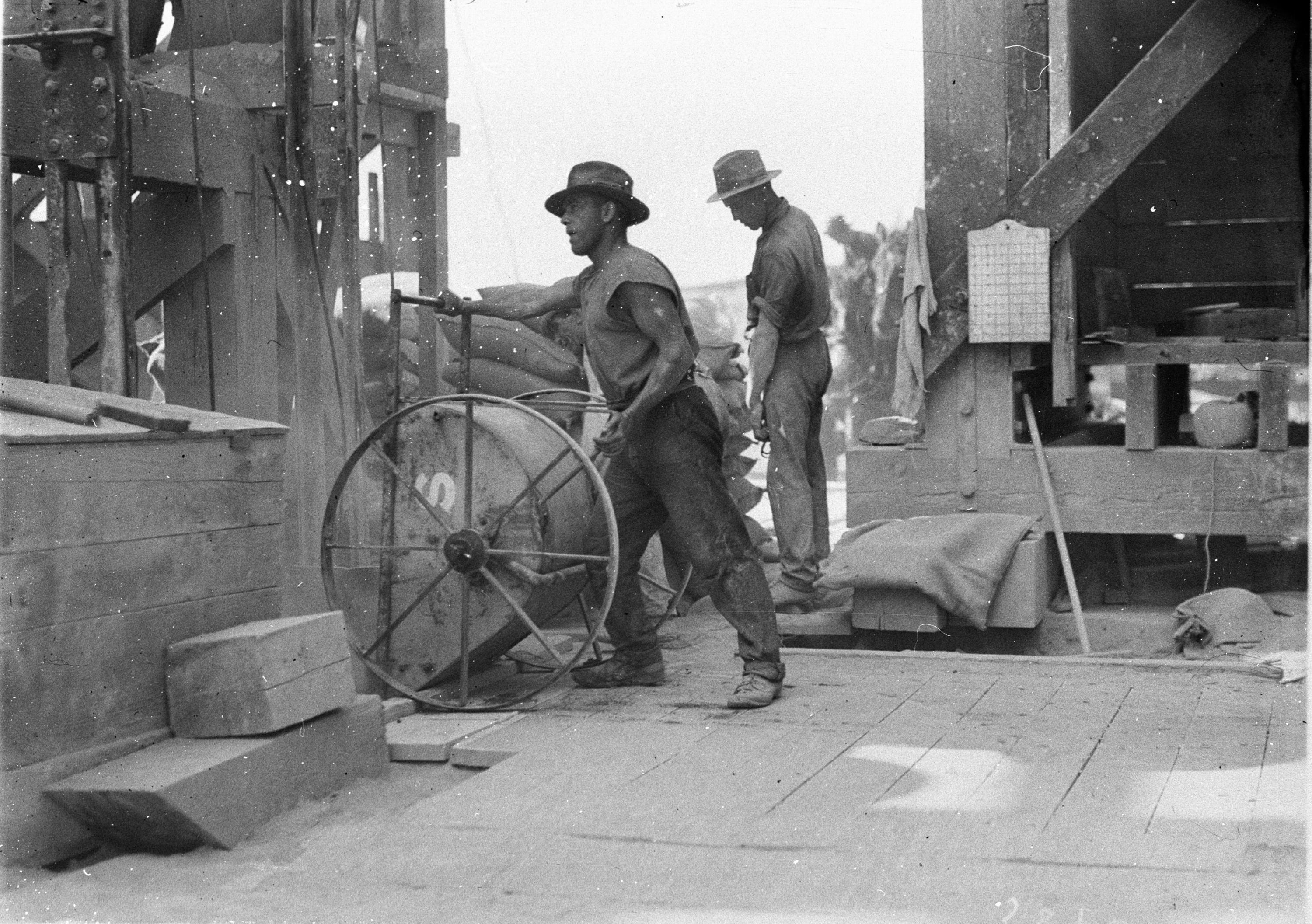 Workmen mixing and pouring concrete with small hand-wheeled hoppers Creator Hood, Ted, 1911-2000, Call Number, Home and Away - 2262 Digital Order No. hood_02262