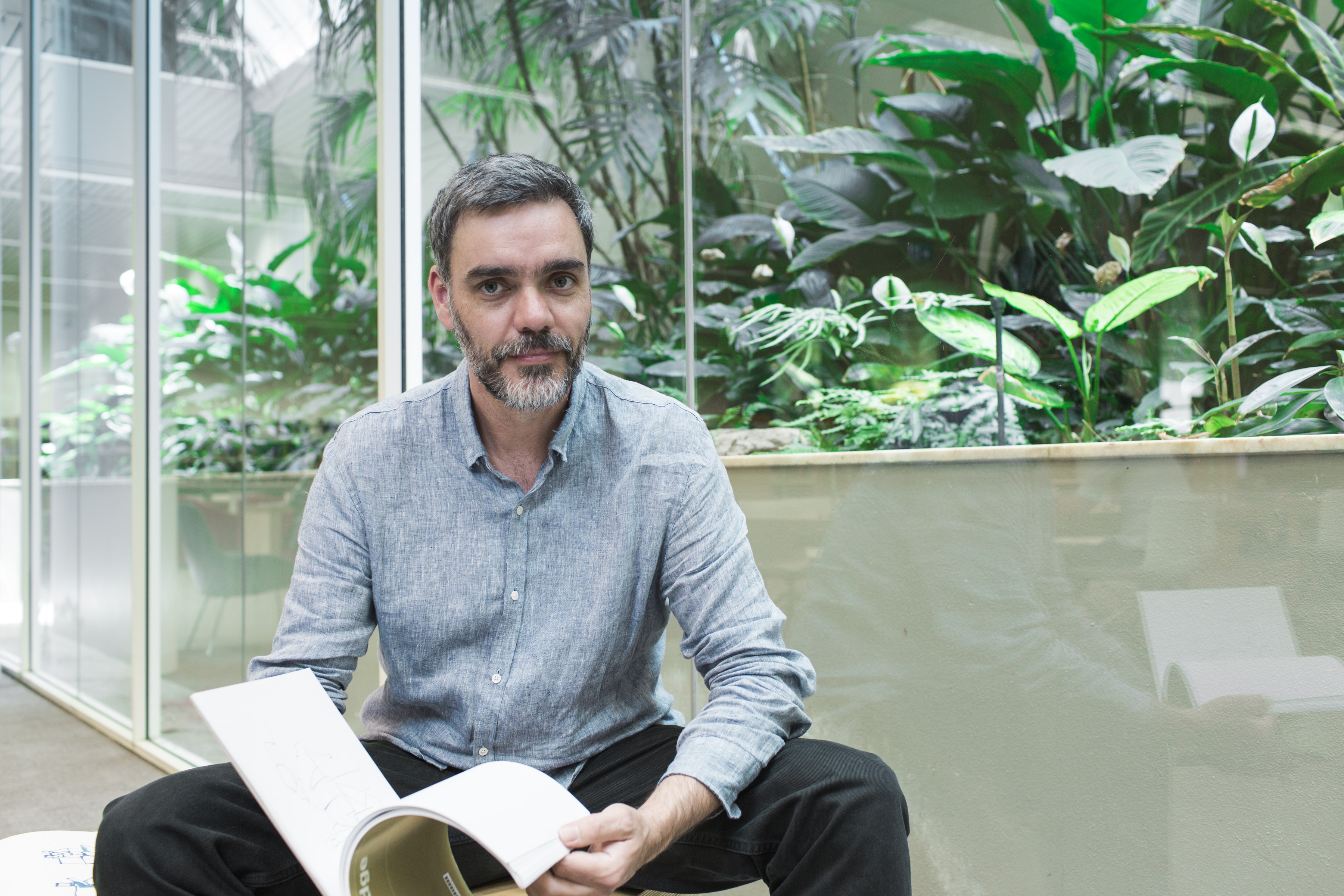 Joe Frost, State Library 'artist in residence', sitting with a book in hand, in the Governor Marie Bashir Reading Room.
