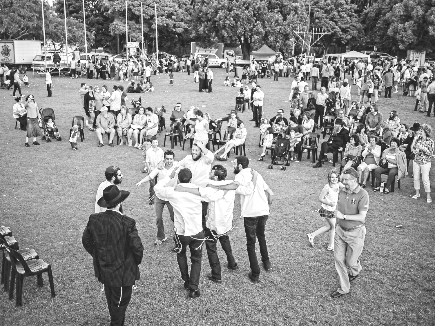 Men and women dance in a park at a community event with a crowd of people watching on.