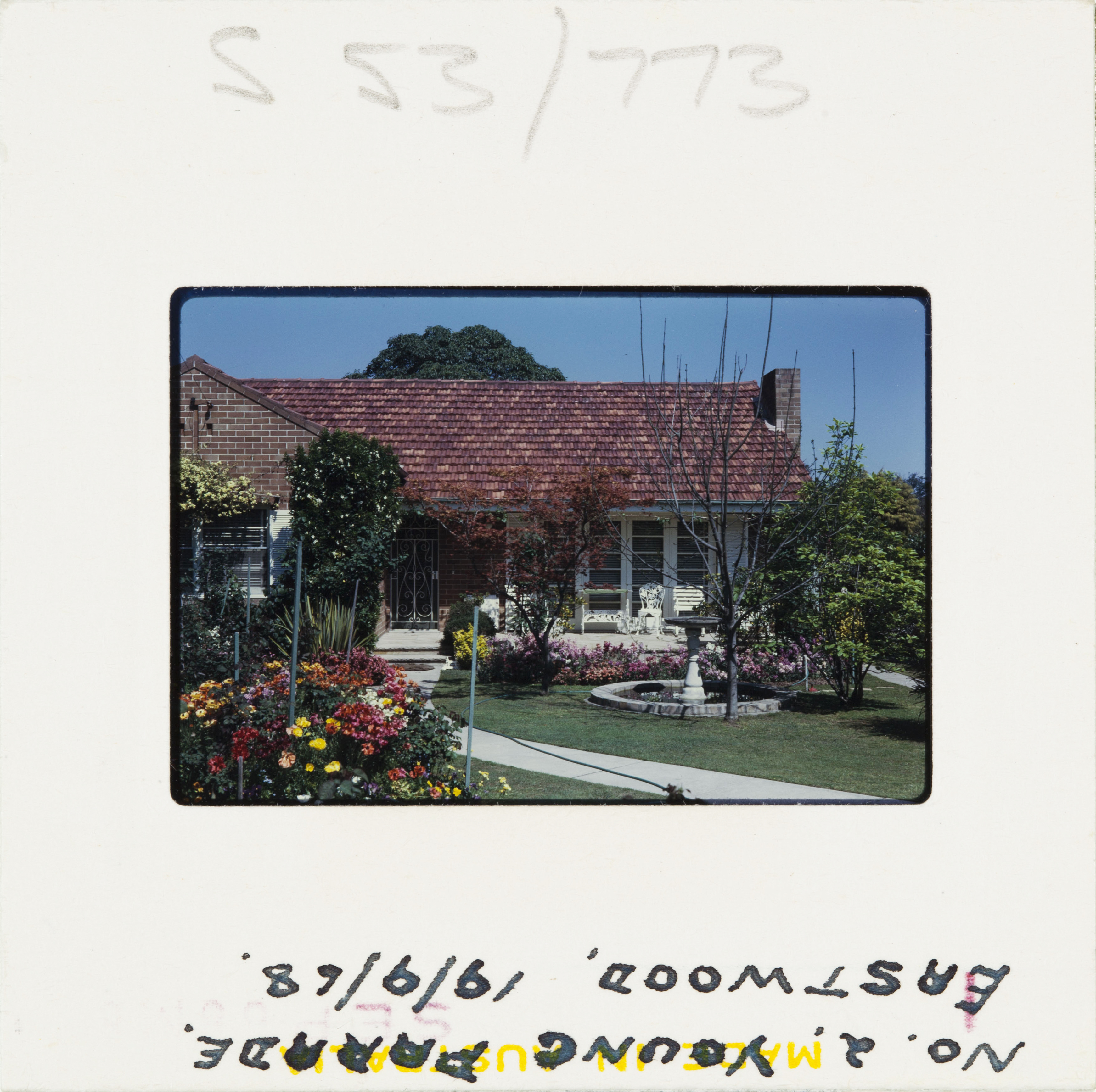 A 60s Kodak colour slide of a suburban brick home with colourful front garden in full flower.