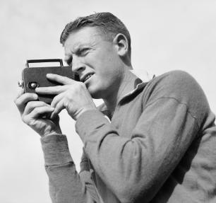 Black and white image of man holding camera to eye