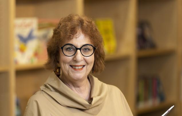 A woman wearing glasses smiling and holding a book