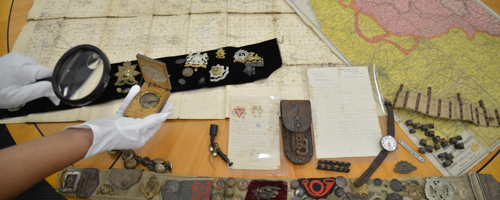 A pair of hands in white gloves inspecting various WWI items. 