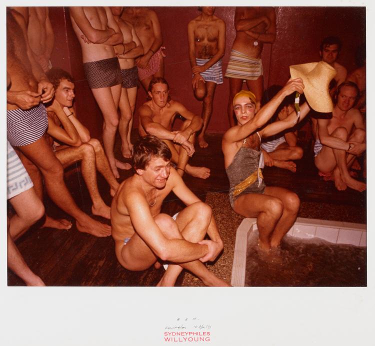 Colour photograph of men sitting and standing around a indoor pool.