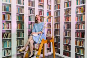 A person sits on a ladder in front of walls of books