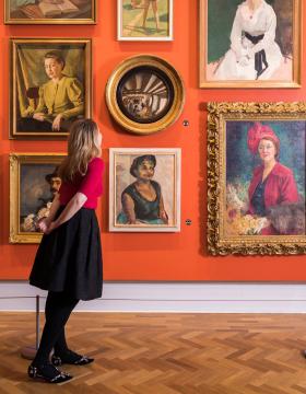 A woman is looking at round painting in the middle of various other paintings
