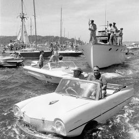 Men in car in water surrounded by boats