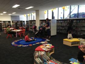 People in a children's area in a library with bookshelves, tables and chairs
