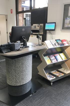 A library service desk stand, next to a shelf with wheels.