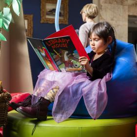 A child is sitting on a bean bag and reading a book