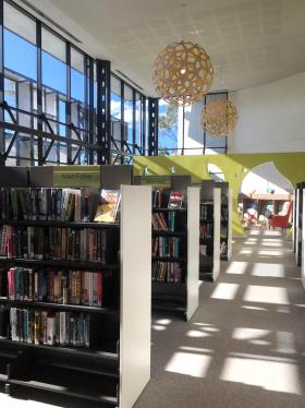 Internal view of library with bookshelves and pendant lights.