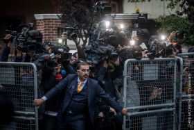 A man opening a gate with a swarm of reporters and photographers behind him. 