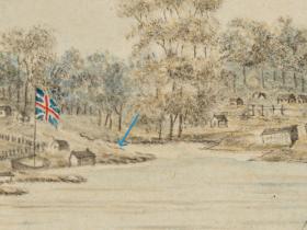 A flag on a pole on the shore of Sydney Cove, with small huts, trees and fences in the background