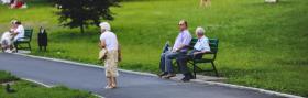 Elderly lady walking in park with two elderly men sitting