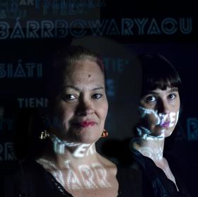 Two women, lit up by projected words.