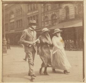 Sepia photograph of three people walking down a cit street wearing masks. 
