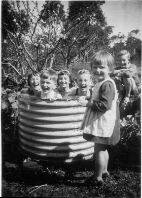 A group of young children bathe in a metal water tub