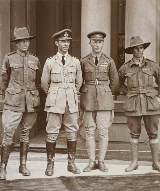 Black and white photograph of four soldiers standing in front of a sandstone building posing for the camera.