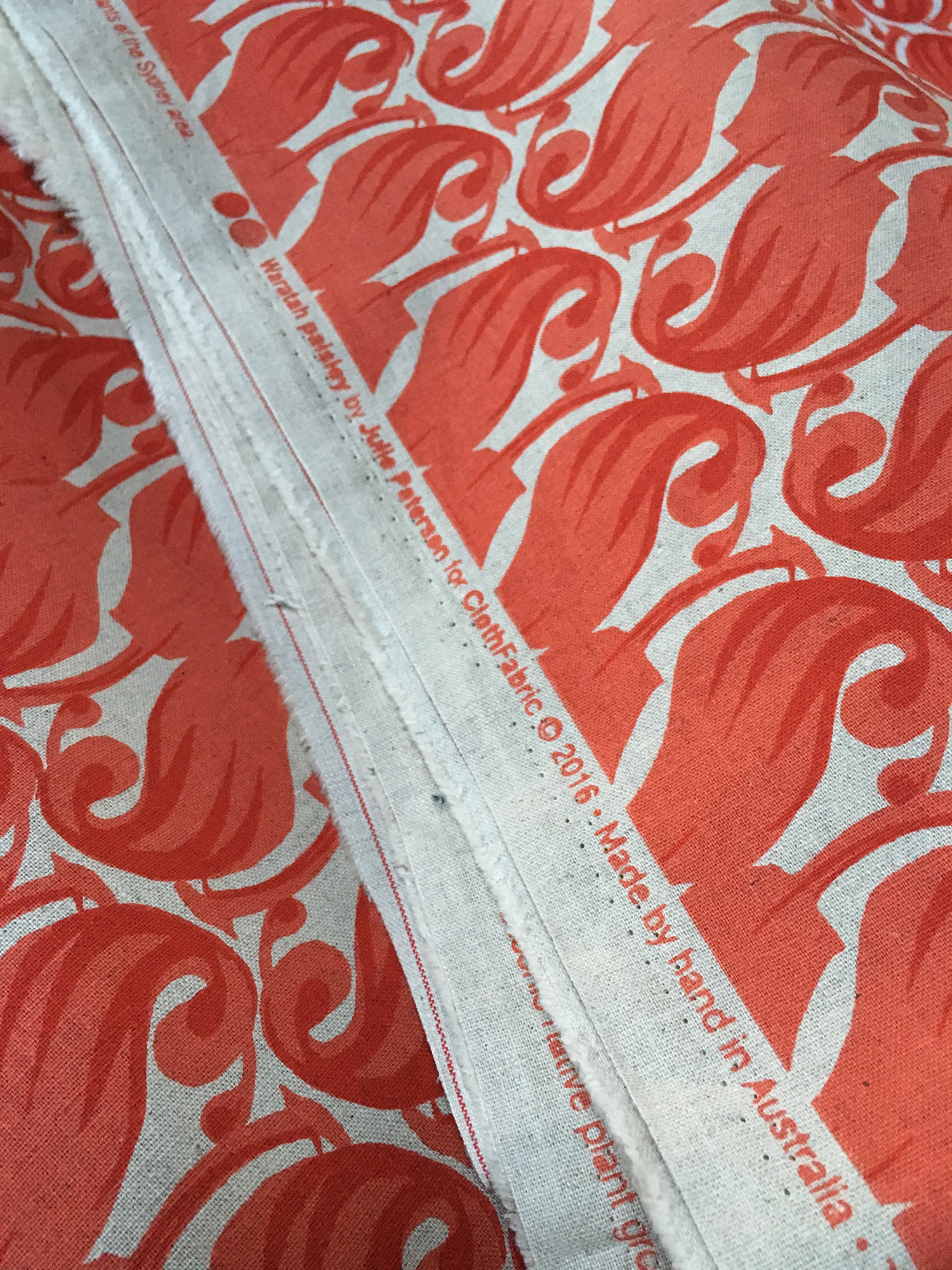 edge of piece of fabric with red print of waratah bud