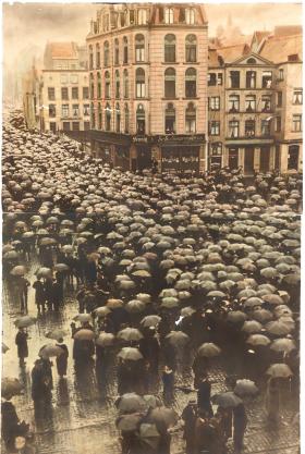 A photograph of a city street, crowded with people holding black umbrellas 