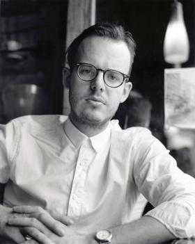 A black and white photo of a man wearing a white button up shirt and black glasses
