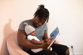 Man reading a book to a baby in his lap. 
