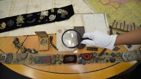 A person wearing a glove hold a magnifying glass over an array of objects